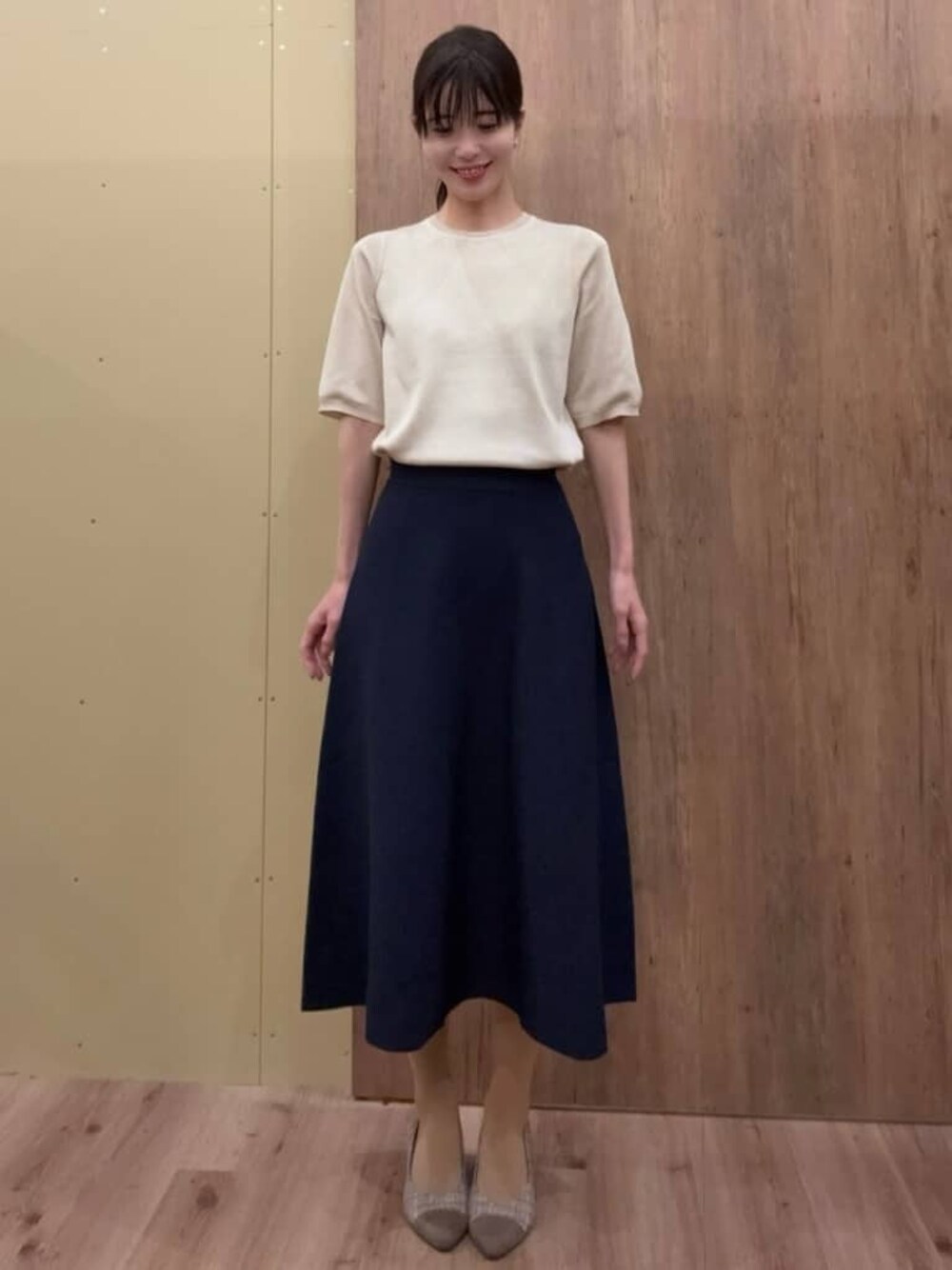 ブラウン系のパンプス、ブルー系のスカート、ゴールド系のニット/セーターを着用したレディースの春コーディネートの1枚目の写真
