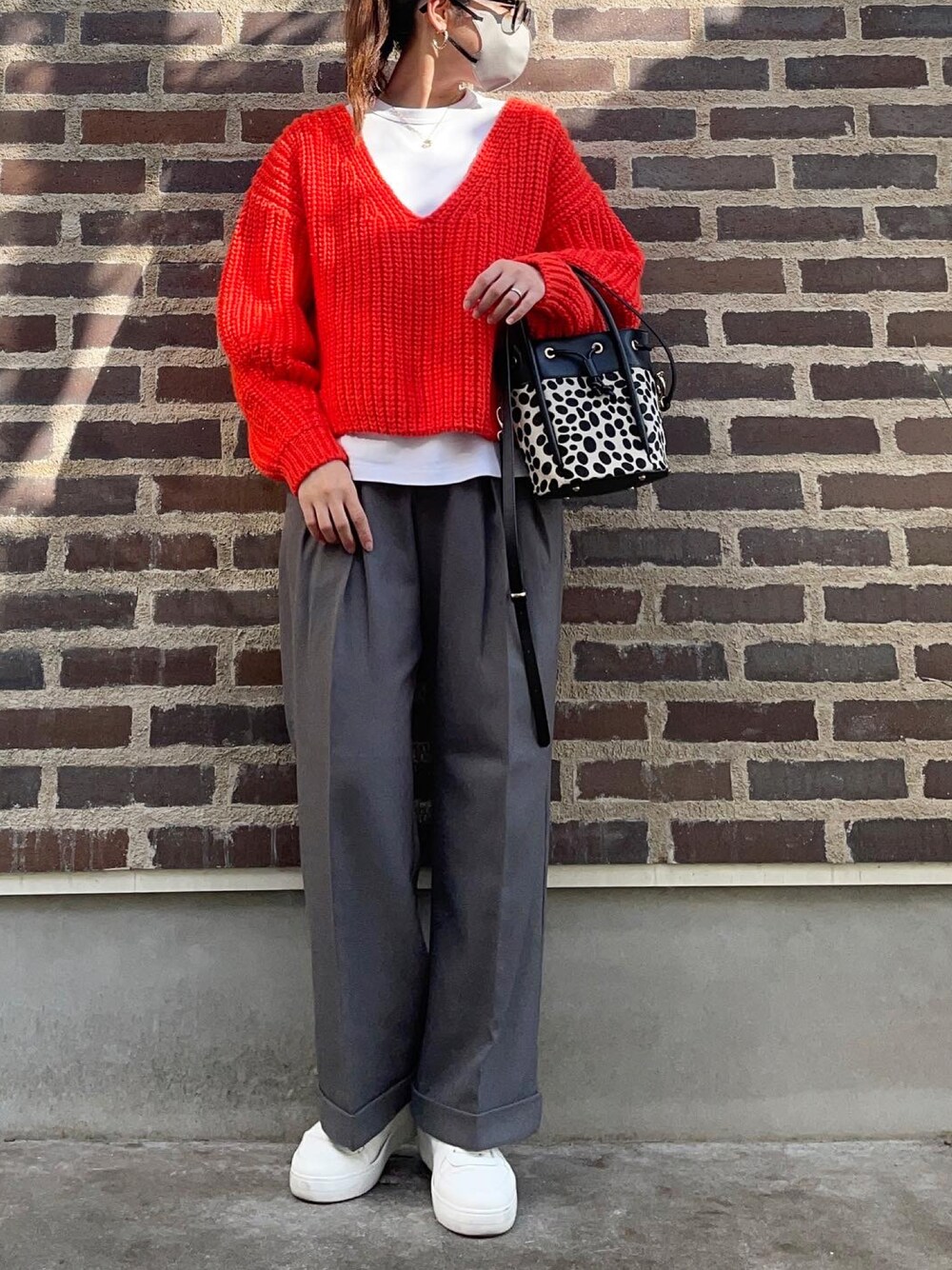 オレンジ系のニット/セーター、グレー系のスラックス、ホワイト系のスニーカーを着用したレディースの秋コーディネートの1枚目の写真