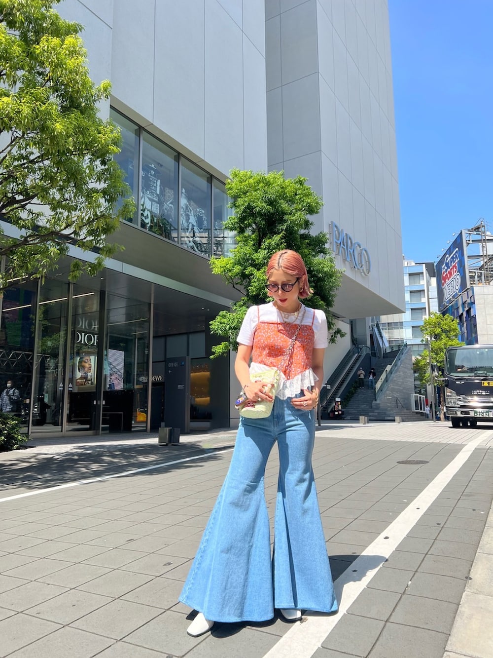 オレンジ系のキャミソール、その他のトートバッグ、ブルー系のデニムパンツを着用したレディースの夏コーディネートの2枚目の写真