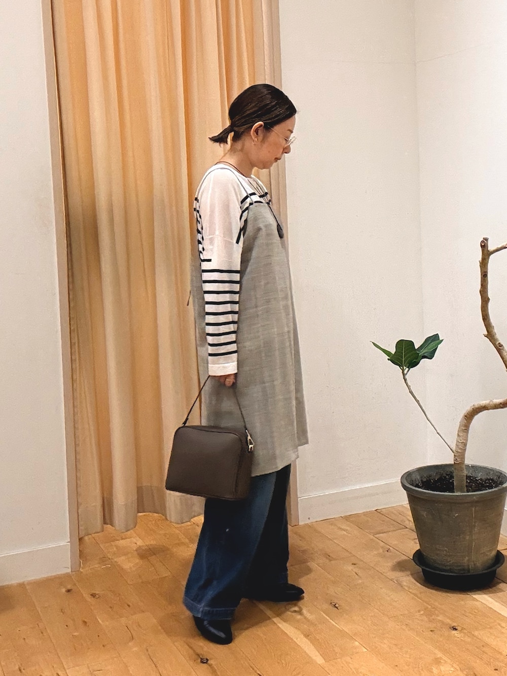グレー系のワンピース、ブルー系のデニムパンツ、ブラウン系のショルダーバッグを着用したレディースの秋コーディネートの4枚目の写真