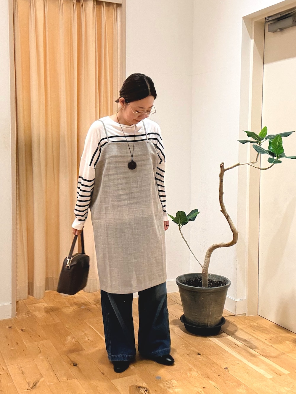 グレー系のワンピース、ブルー系のデニムパンツ、ブラウン系のショルダーバッグを着用したレディースの秋コーディネートの2枚目の写真