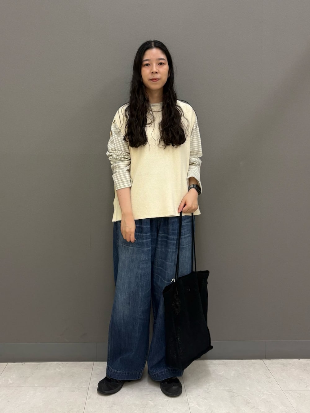 ホワイト系のベスト、ブルー系のデニムパンツ、ブラック系のトートバッグを着用したレディースの秋コーディネートの2枚目の写真