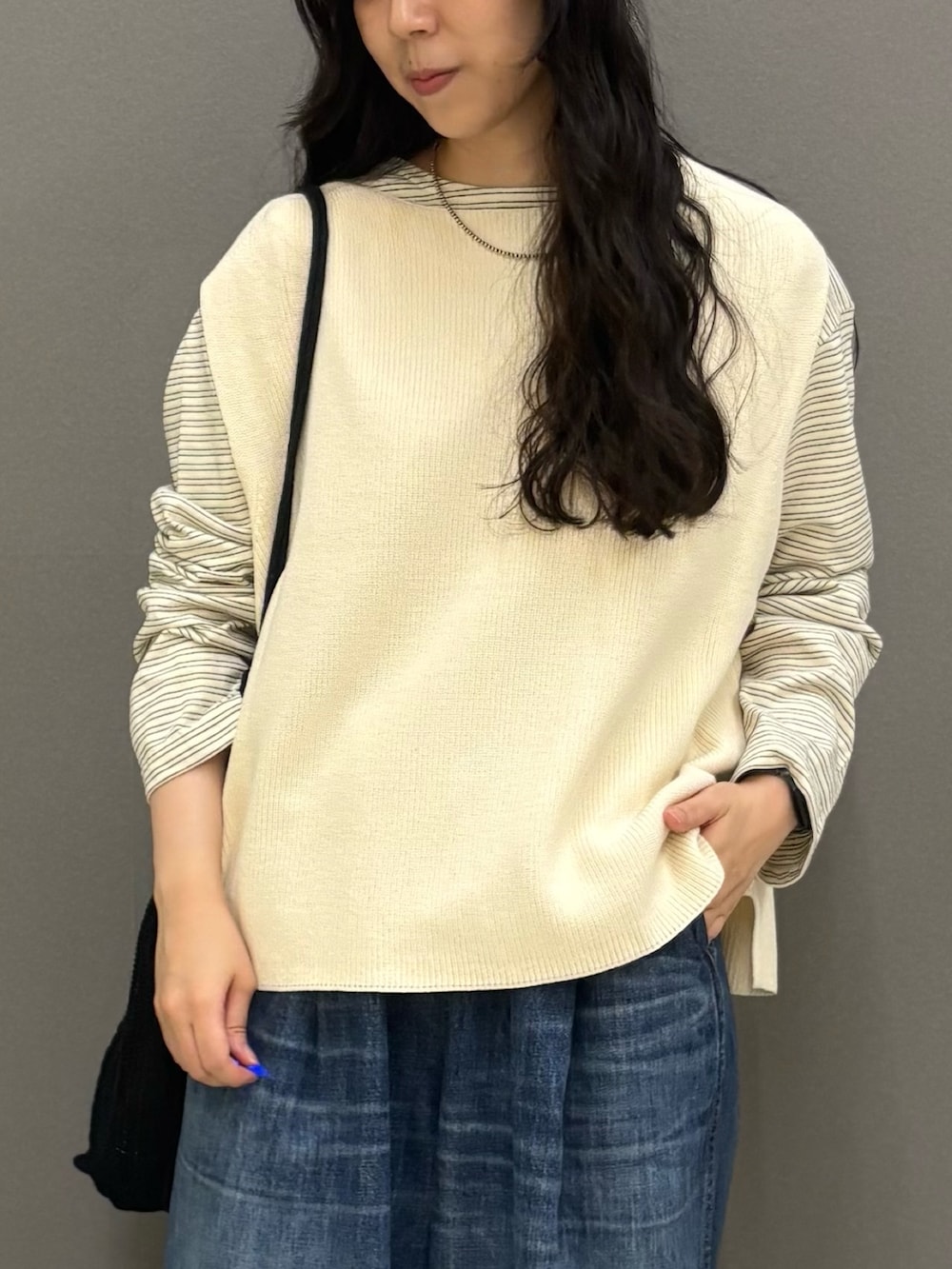 ホワイト系のベスト、ブルー系のデニムパンツ、ブラック系のトートバッグを着用したレディースの秋コーディネートの3枚目の写真