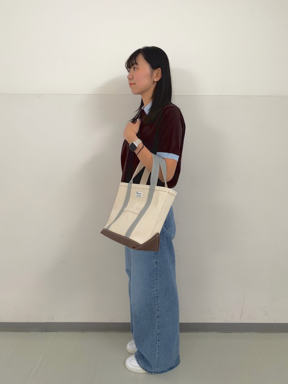 ブラウン系のニット/セーター、グリーン系のトートバッグ、ブルー系のデニムパンツを着用したレディースの春コーディネートの2枚目の写真