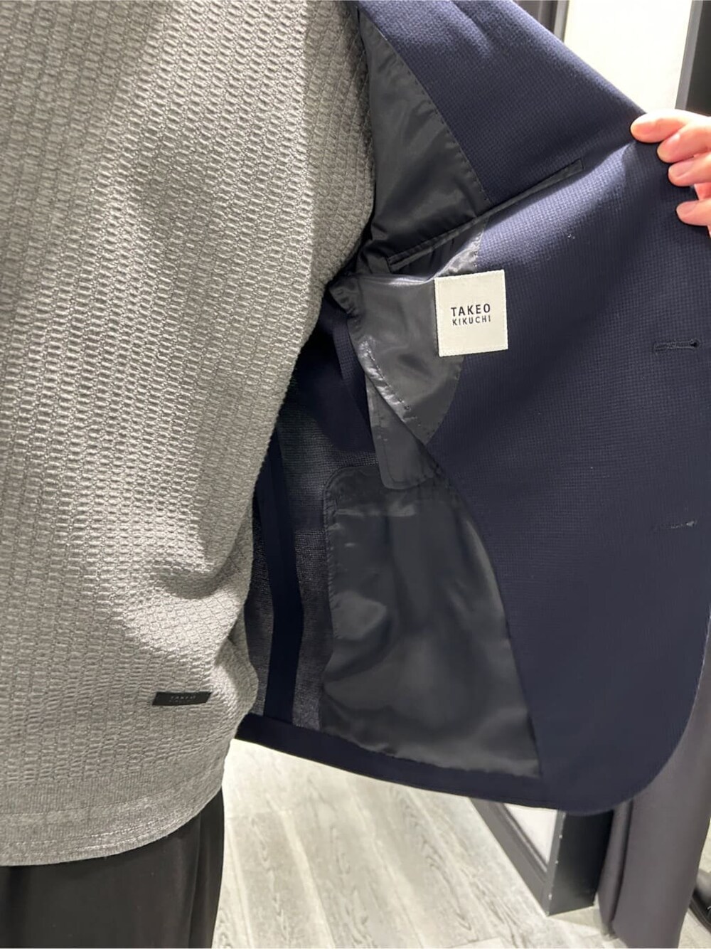 グレー系のニット/セーター、ブルー系のテーラードジャケット、グレー系のショルダーバッグを着用したメンズの秋コーディネートの6枚目の写真