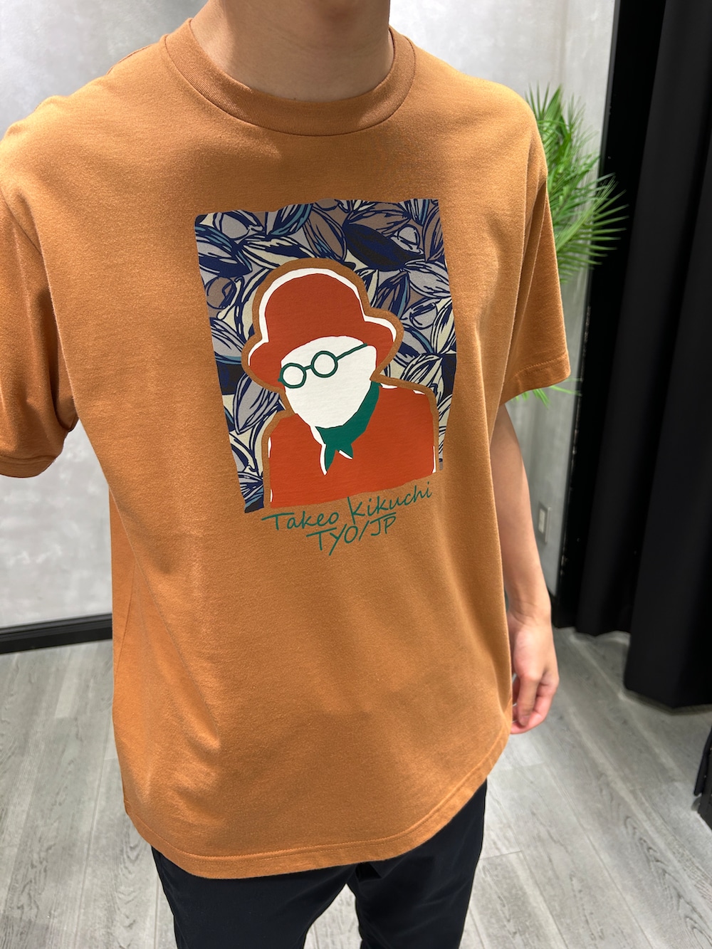 オレンジ系のTシャツ/カットソー、ブルー系のスラックス、ブルー系のトートバッグを着用したメンズの夏コーディネートの4枚目の写真