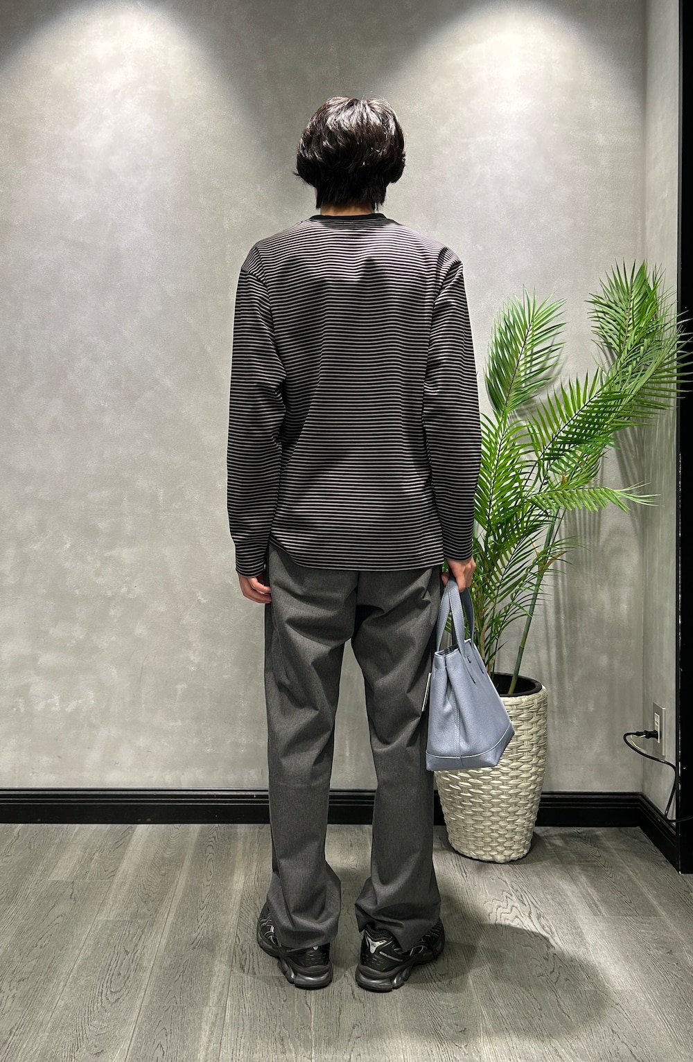 ブラック系のTシャツ/カットソー、グレー系のスラックス、ブルー系のトートバッグを着用したメンズの秋コーディネートの3枚目の写真