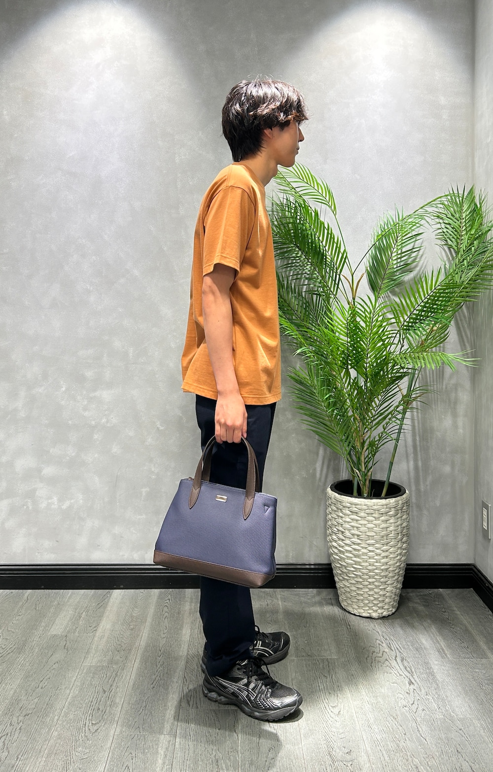 オレンジ系のTシャツ/カットソー、ブルー系のスラックス、ブルー系のトートバッグを着用したメンズの夏コーディネートの2枚目の写真