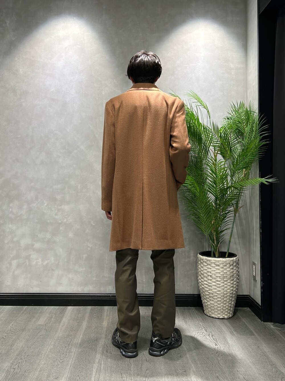 ブラウン系のステンカラーコート、グレー系のTシャツ/カットソー、グリーン系のスラックスを着用したメンズの冬コーディネートの3枚目の写真