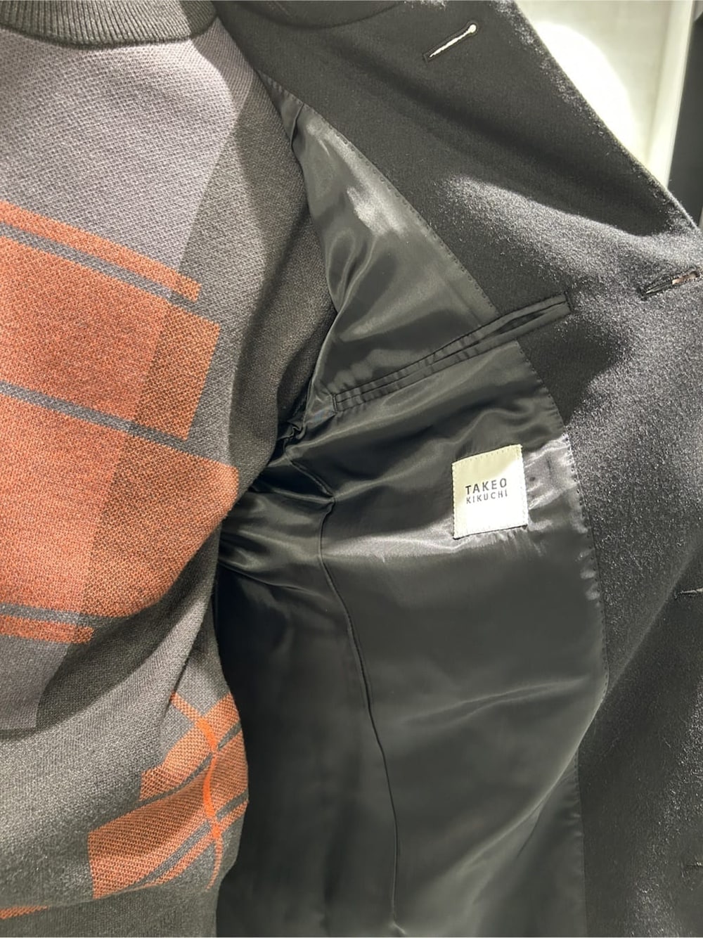 ブラック系のステンカラーコート、グレー系のニット/セーター、ブラック系のスラックスを着用したメンズの冬コーディネートの5枚目の写真