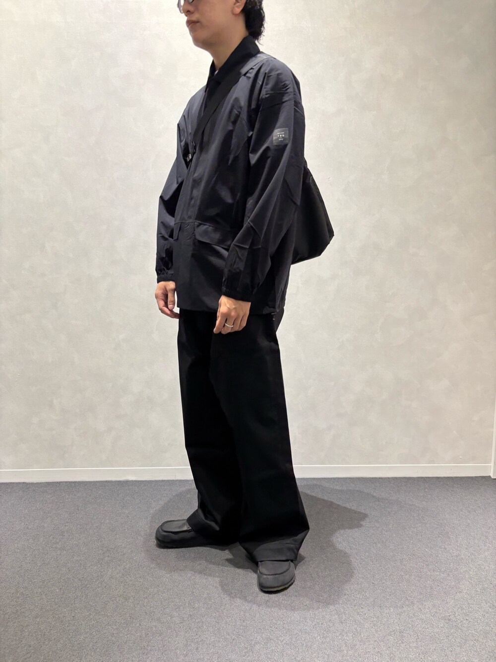 ブラック系のチノパンツ、ブラック系のショルダーバッグ、ブラック系のレインコート/ポンチョを着用したメンズの春コーディネートの3枚目の写真