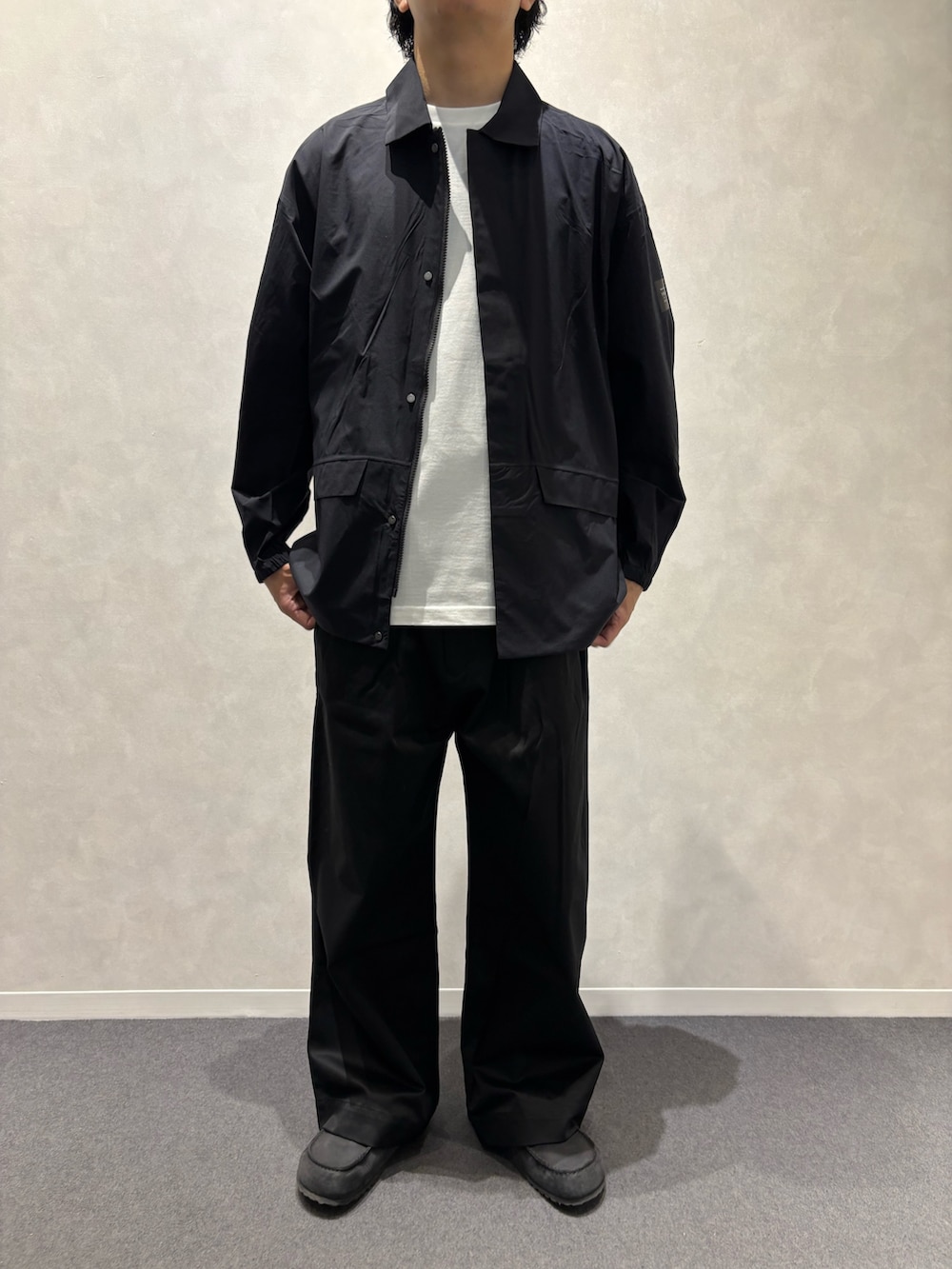 ブラック系のチノパンツ、ブラック系のショルダーバッグ、ブラック系のレインコート/ポンチョを着用したメンズの春コーディネートの5枚目の写真
