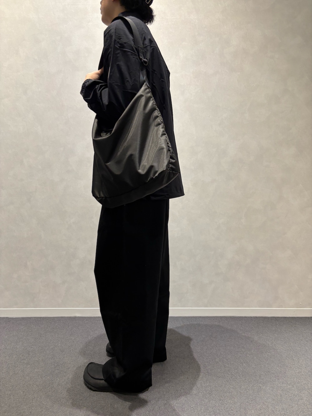 ブラック系のチノパンツ、ブラック系のショルダーバッグ、ブラック系のレインコート/ポンチョを着用したメンズの春コーディネートの4枚目の写真
