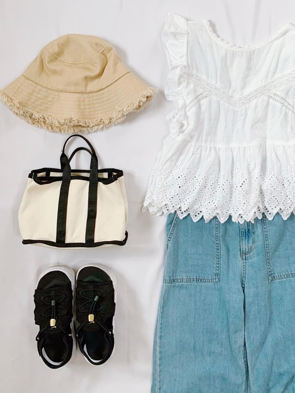 ホワイト系のトートバッグ、ブラック系のサンダル、ブルー系のデニムパンツを着用したレディースの夏コーディネートの2枚目の写真