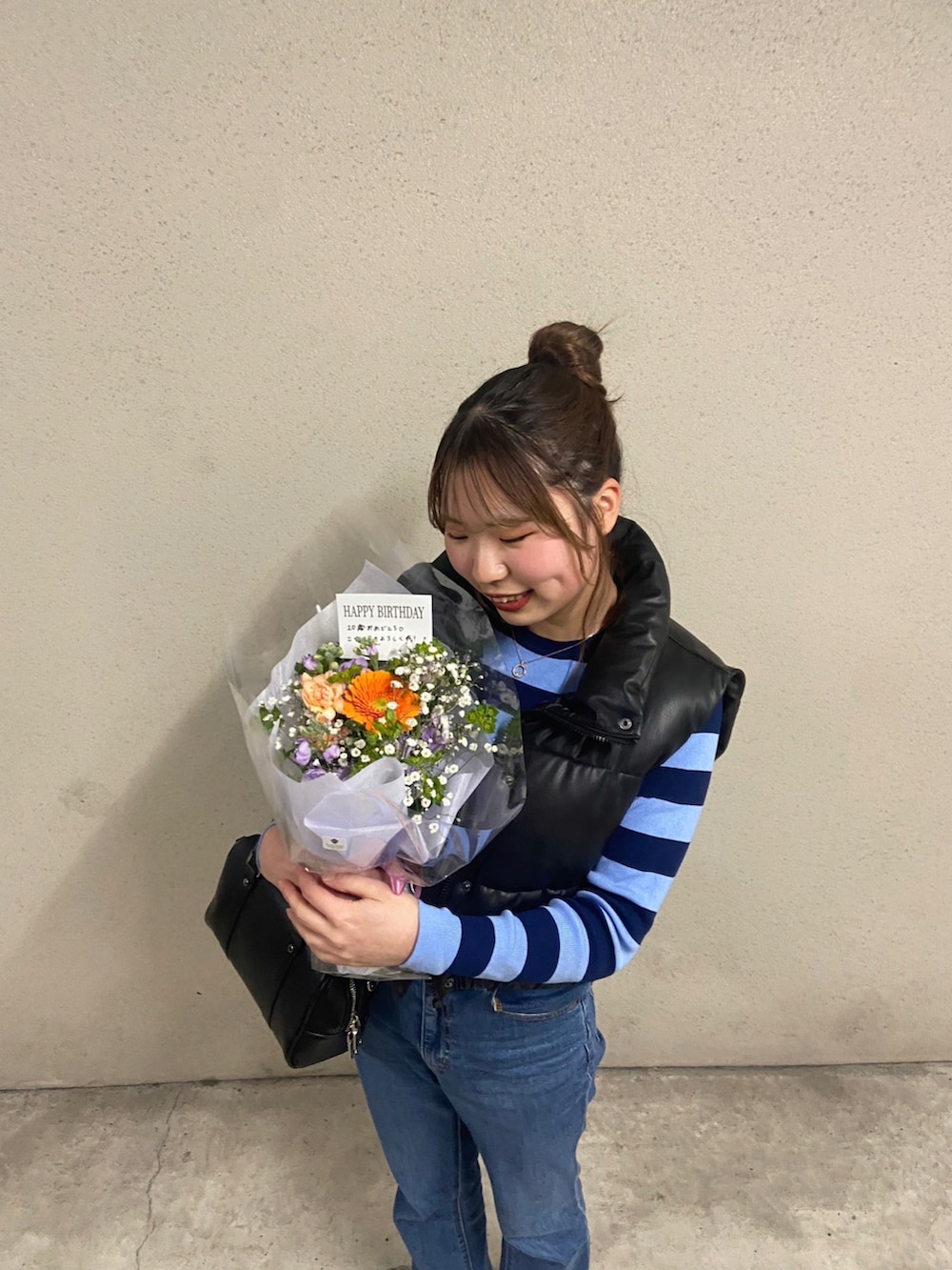 ブラック系のバッグ、ブルー系のデニムパンツ、ブラック系のダウンベストを着用したレディースの春コーディネートの3枚目の写真