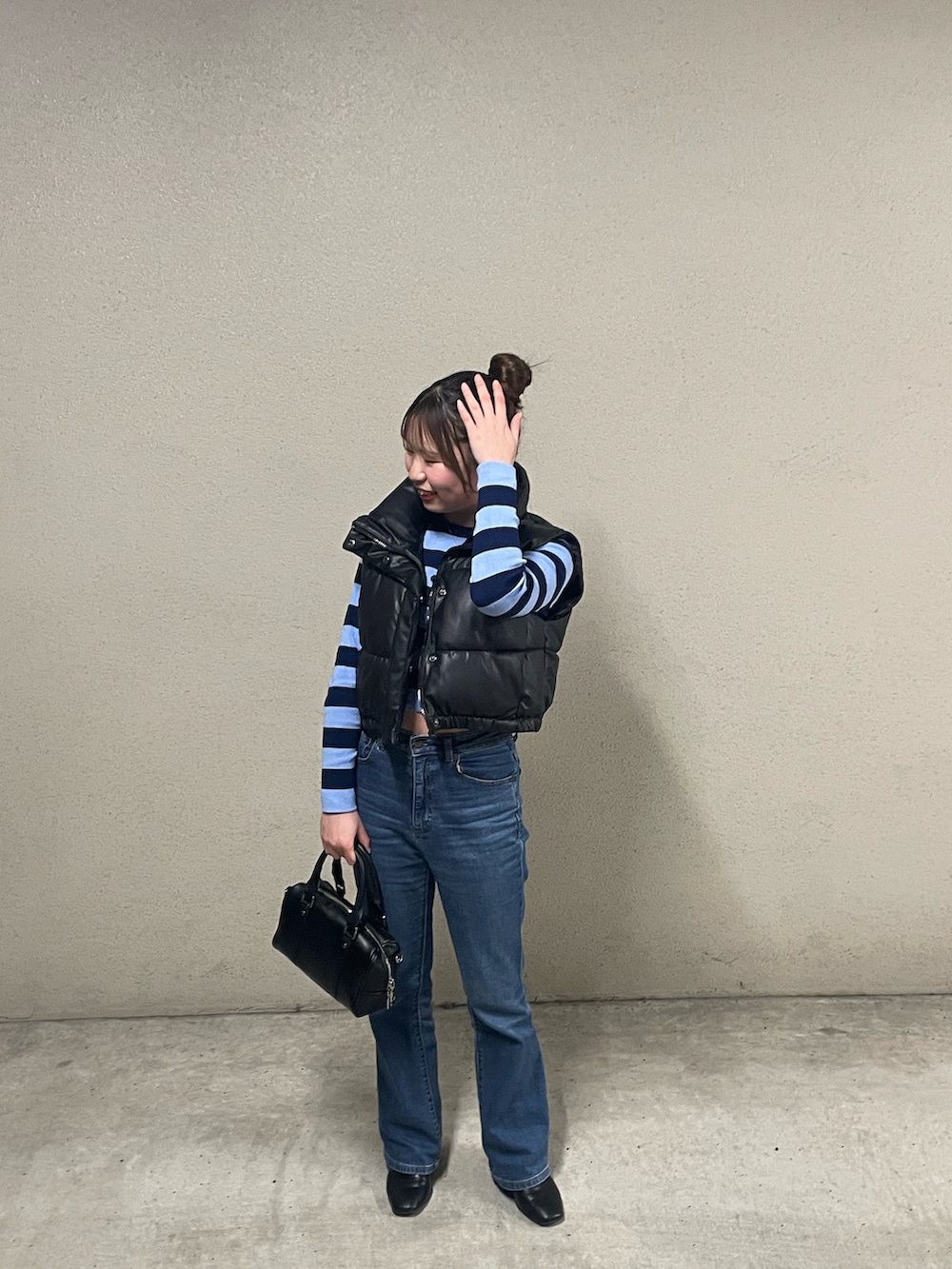 ブラック系のバッグ、ブルー系のデニムパンツ、ブラック系のダウンベストを着用したレディースの春コーディネートの2枚目の写真