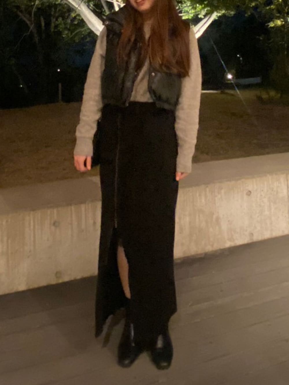 ブラック系のダウンベスト、グレー系のニット/セーター、ブラック系のスカートを着用したレディースの春コーディネートの2枚目の写真