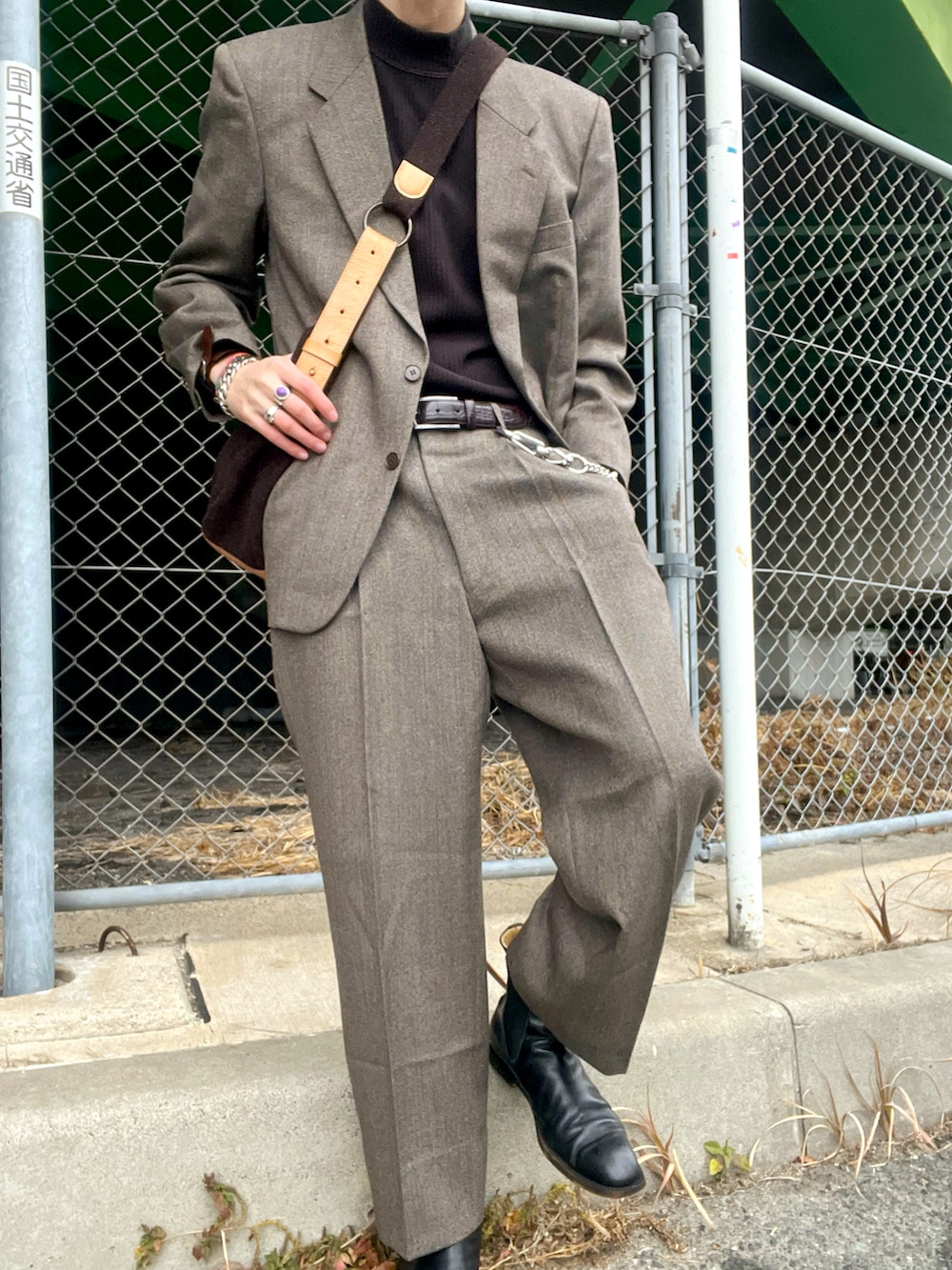 グレー系のスーツジャケット、グレー系のスーツパンツ、ブラウン系のショルダーバッグを着用したメンズの冬コーディネートの2枚目の写真