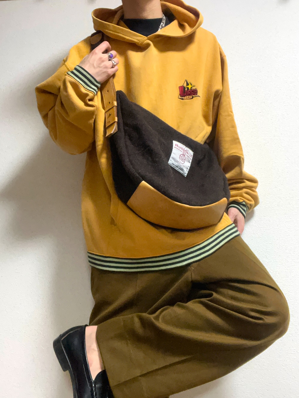 ブラウン系のショルダーバッグ、イエロー系のパーカー、ブラック系のスリッポンを着用したメンズの冬コーディネートの2枚目の写真