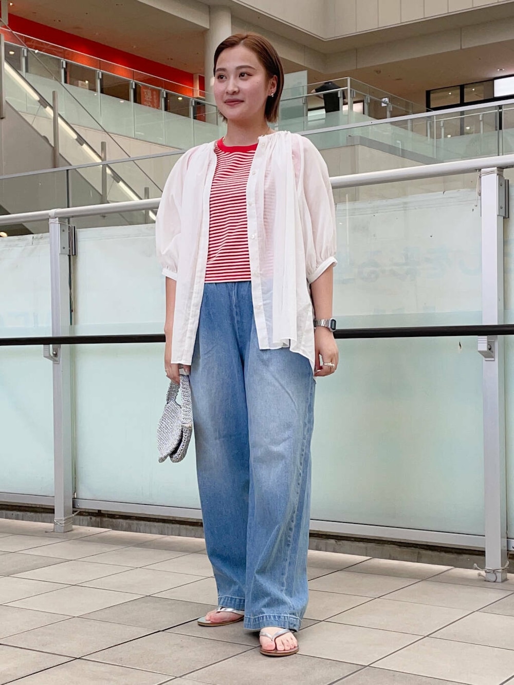 シルバー系のハンドバッグ、シルバー系のサンダル、ブルー系のデニムパンツを着用したレディースの夏コーディネートの2枚目の写真