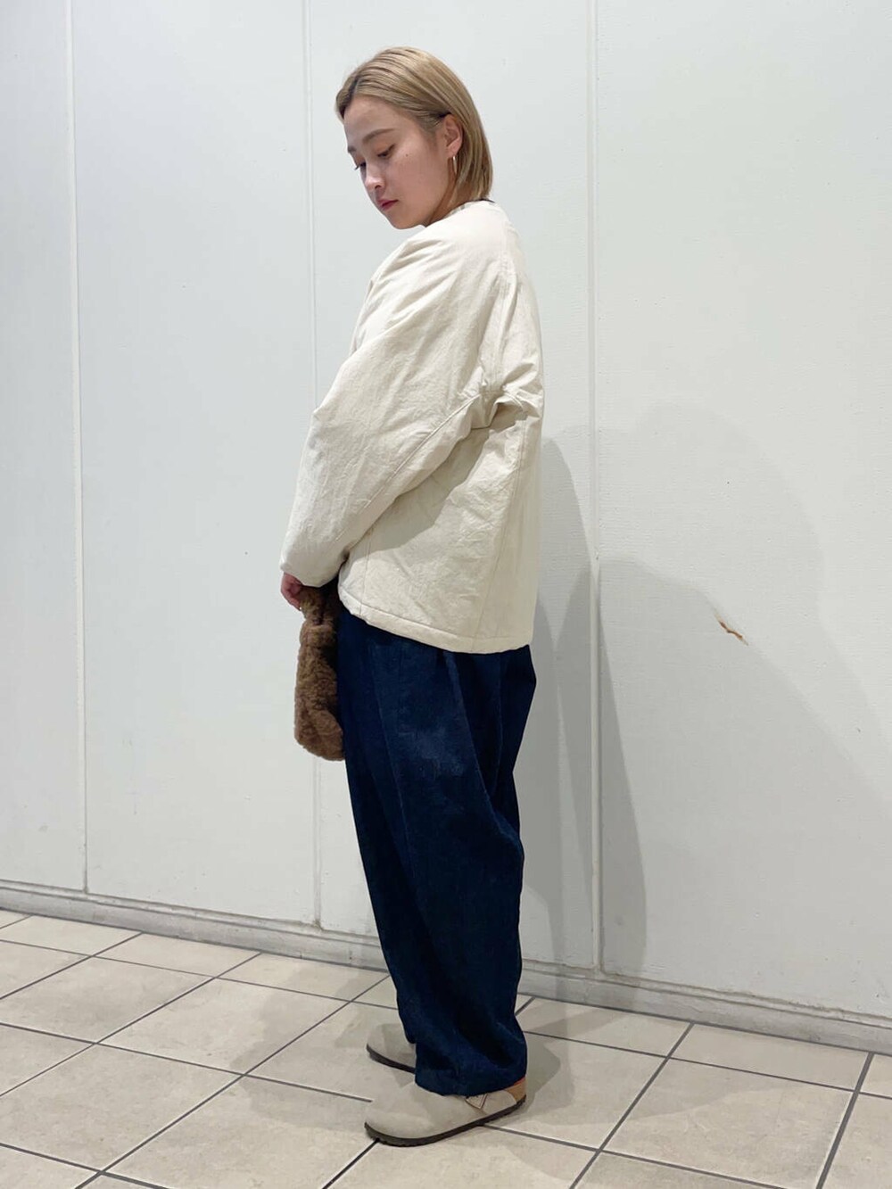 ブルー系のデニムパンツ、ブラウン系のハンドバッグ、ホワイト系のニット/セーターを着用したレディースの秋コーディネートの2枚目の写真
