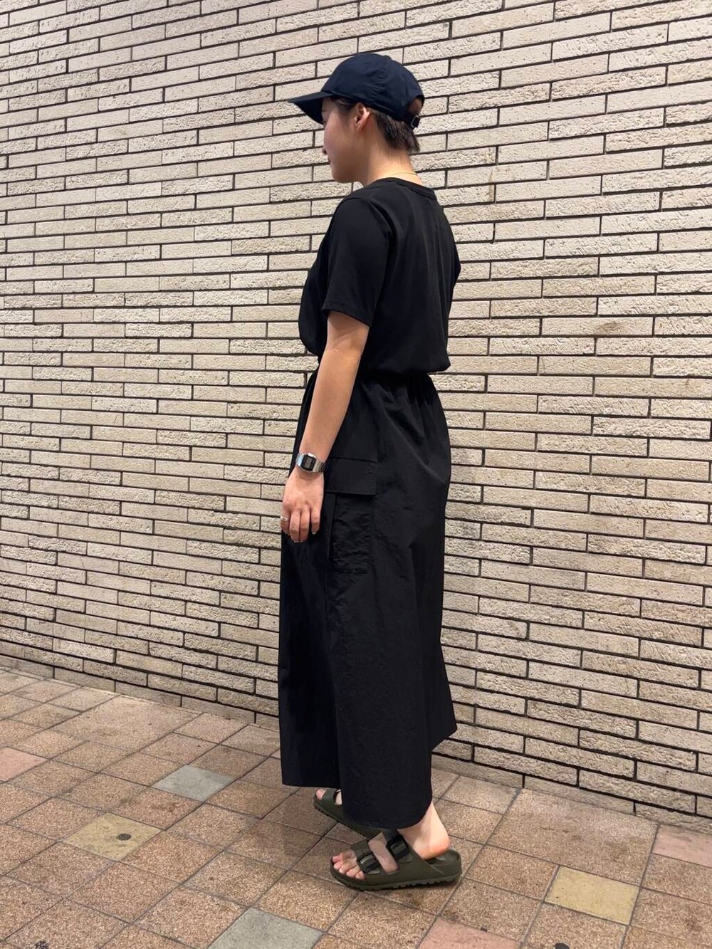 ブラック系のワンピース、グリーン系のサンダル、ブルー系のキャップを着用したレディースの夏コーディネートの3枚目の写真