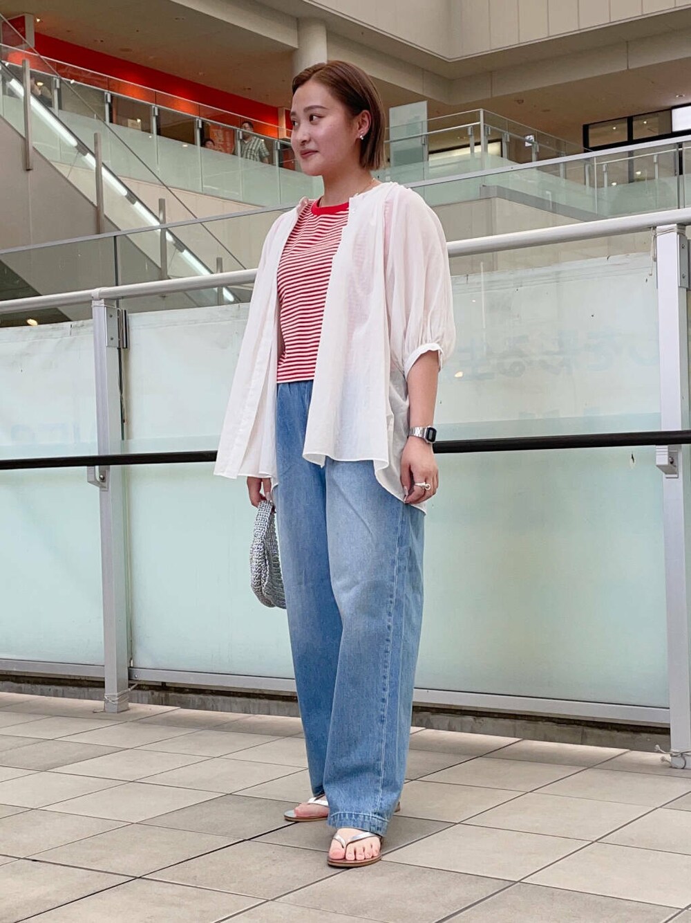 シルバー系のハンドバッグ、シルバー系のサンダル、ブルー系のデニムパンツを着用したレディースの夏コーディネートの3枚目の写真