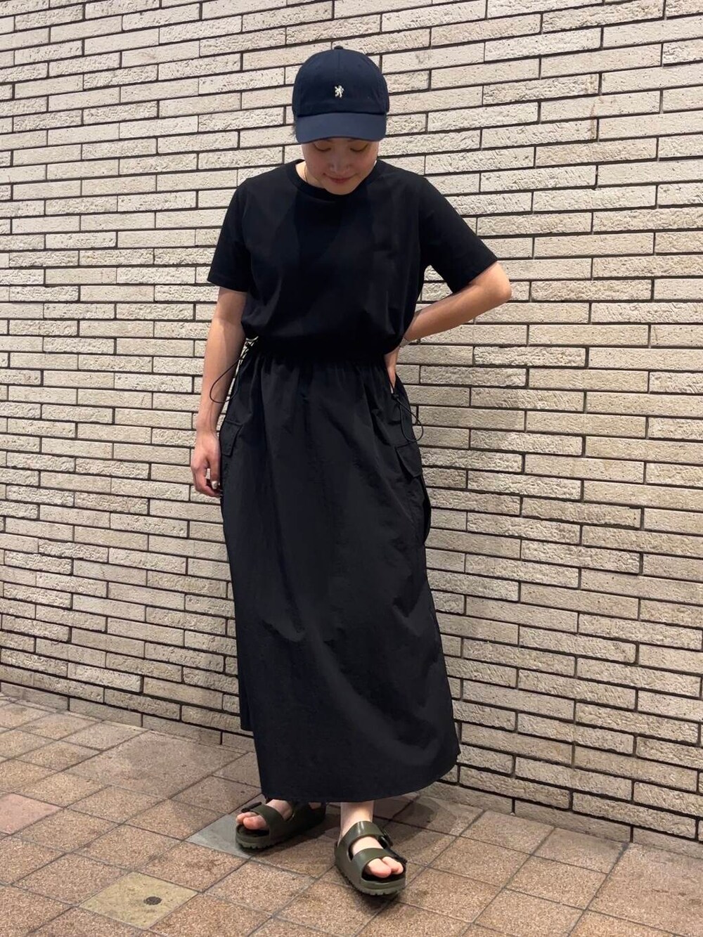 ブラック系のワンピース、グリーン系のサンダル、ブルー系のキャップを着用したレディースの夏コーディネートの2枚目の写真