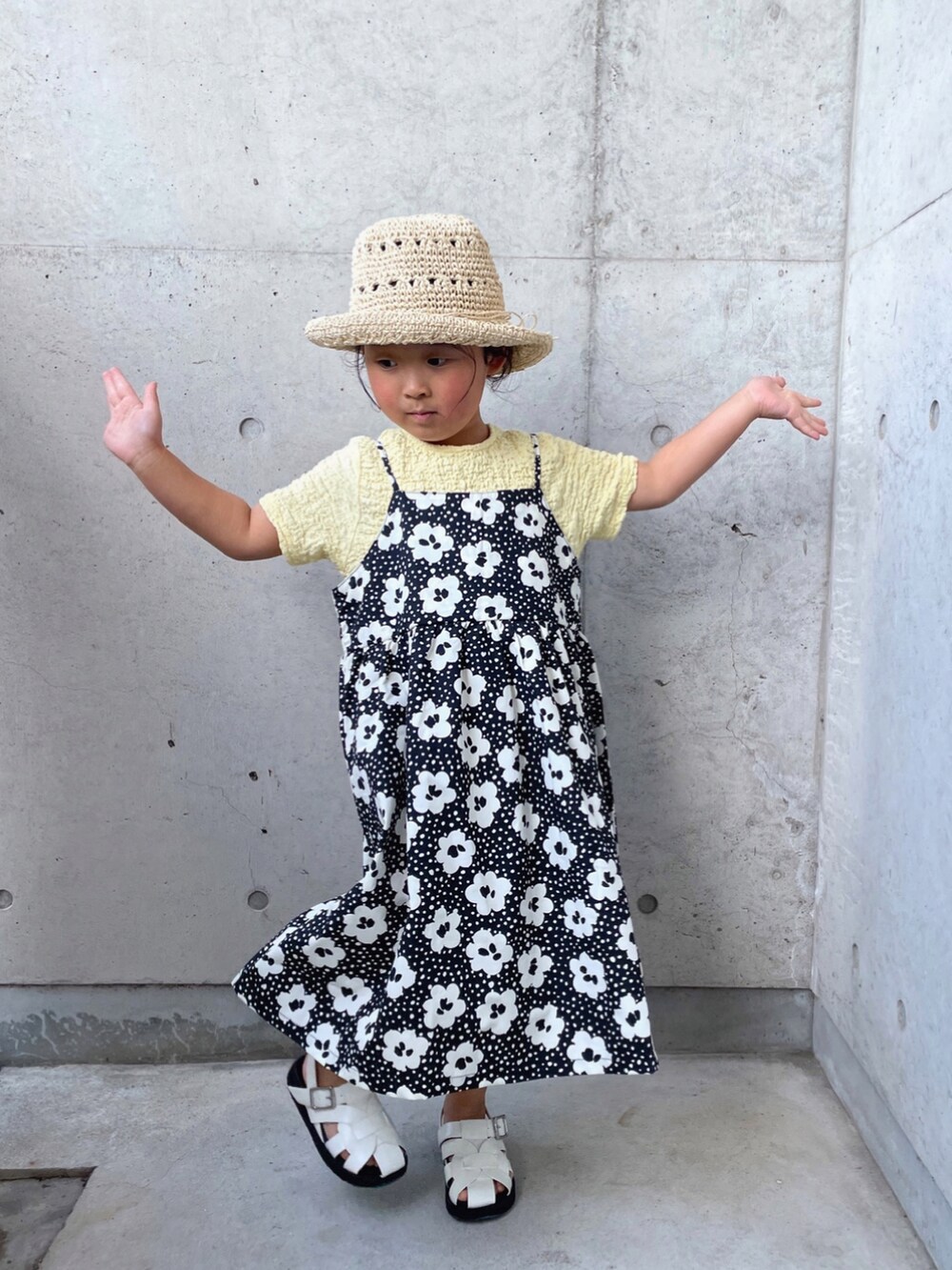 ブラック系のワンピース、ホワイト系のサンダル、ベージュ系のTシャツ/カットソーを着用したキッズの春コーディネートの2枚目の写真