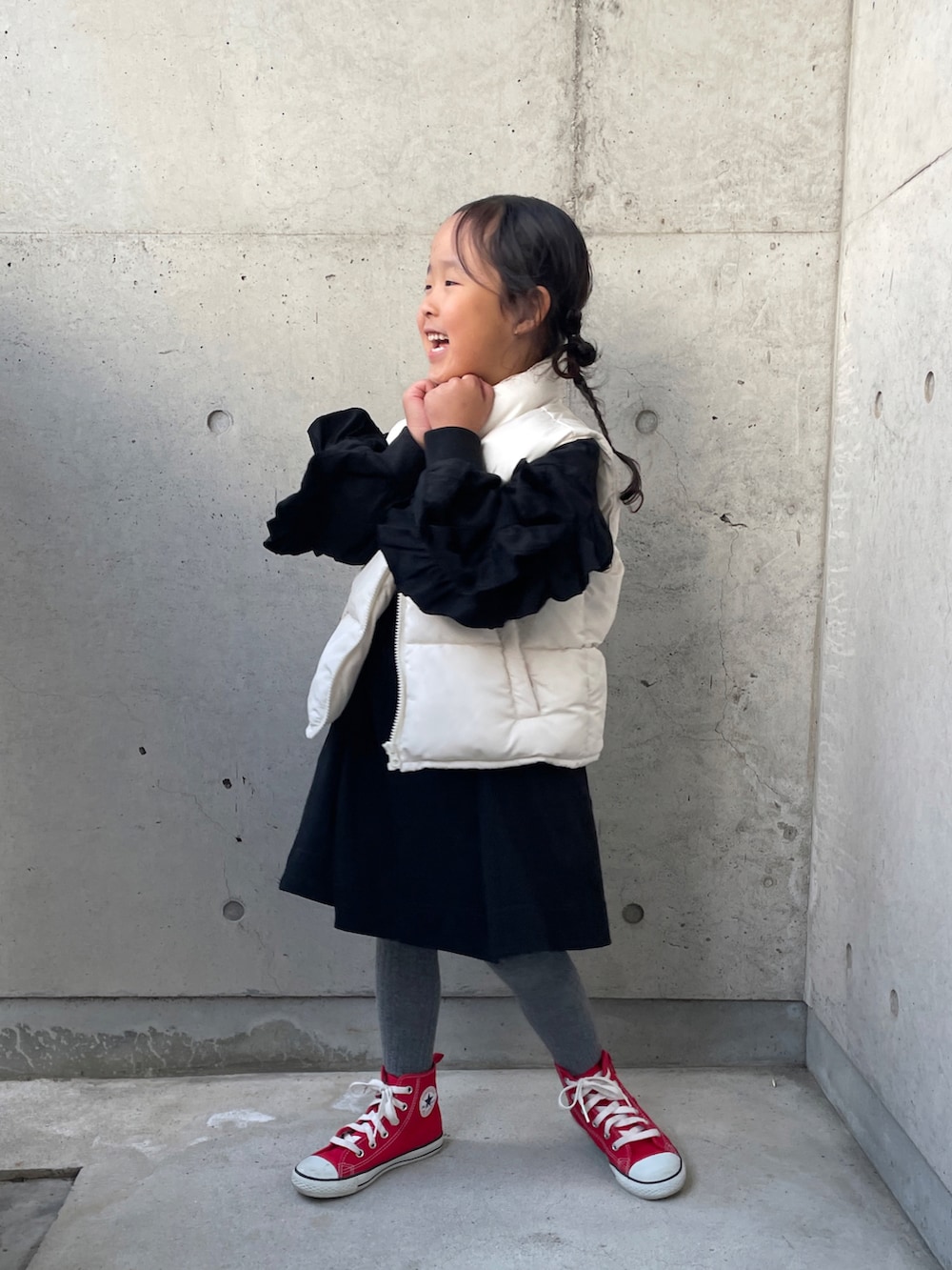 ホワイト系のダウンベスト、ブラック系のワンピース、レッド系のスニーカーを着用したキッズの秋コーディネートの5枚目の写真