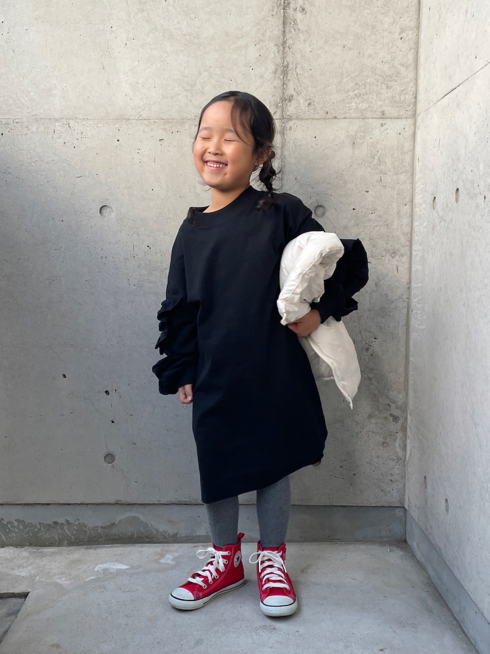 ホワイト系のダウンベスト、ブラック系のワンピース、レッド系のスニーカーを着用したキッズの秋コーディネートの4枚目の写真