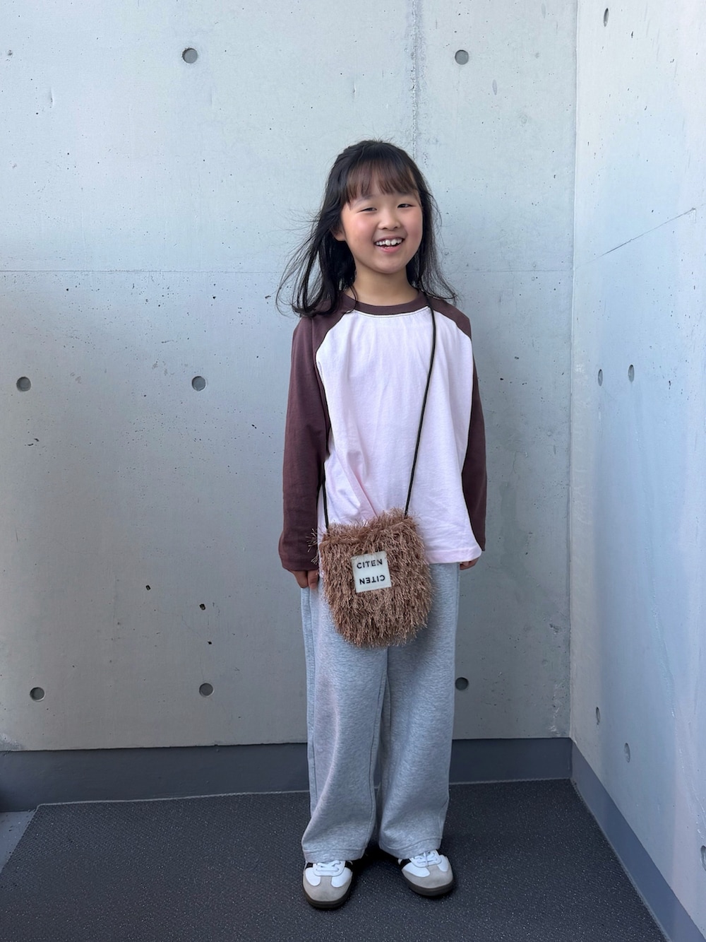 ピンク系のTシャツ/カットソー、ブラウン系のショルダーバッグ、ホワイト系のスニーカーを着用したキッズの秋コーディネートの5枚目の写真