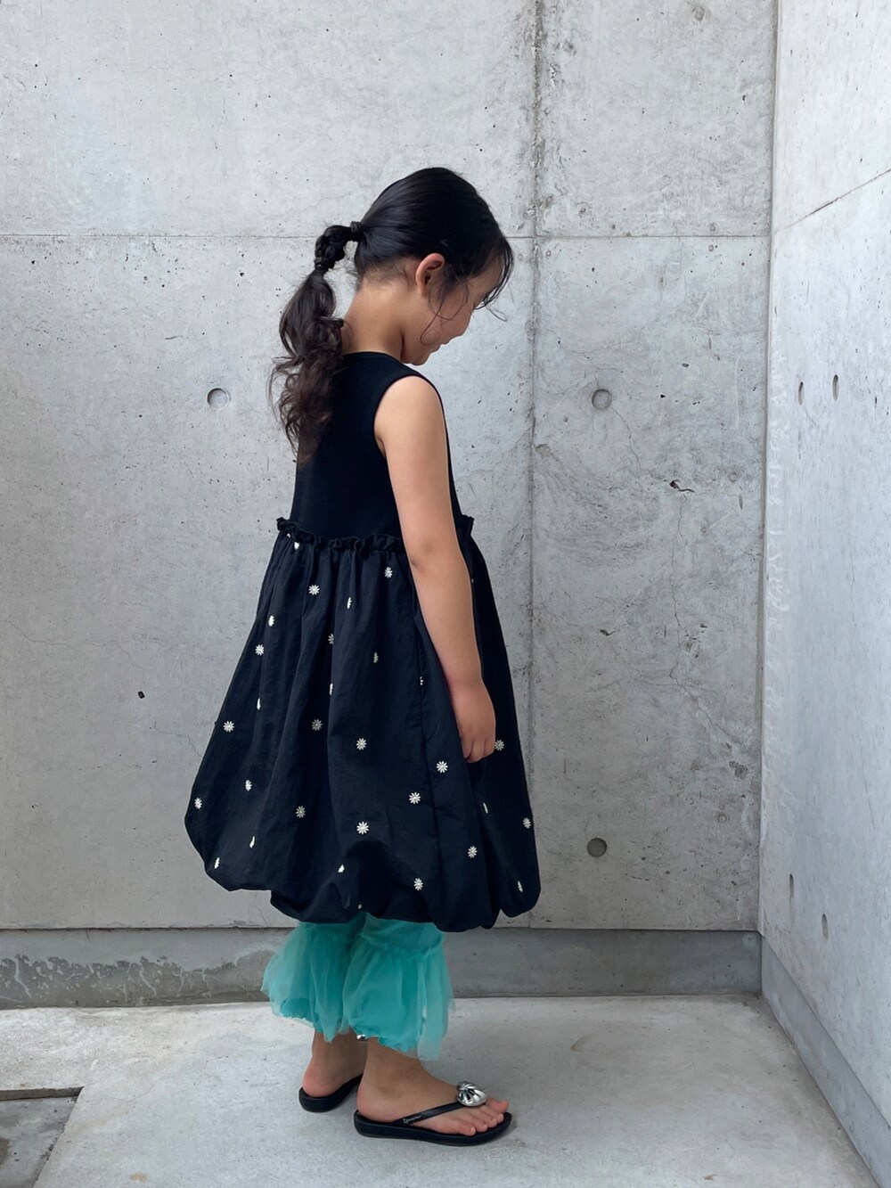 シルバー系のハンドバッグ、ブラック系のワンピース、ブラック系のサンダルを着用したキッズの夏コーディネートの5枚目の写真