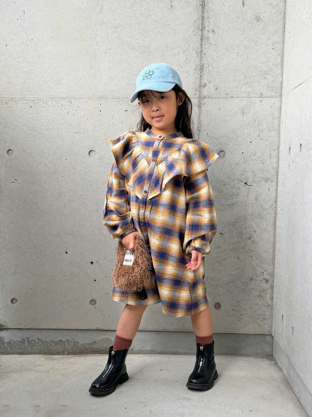 イエロー系のワンピース、ブラウン系のショルダーバッグ、ブラック系のブーツを着用したキッズの秋コーディネートの2枚目の写真