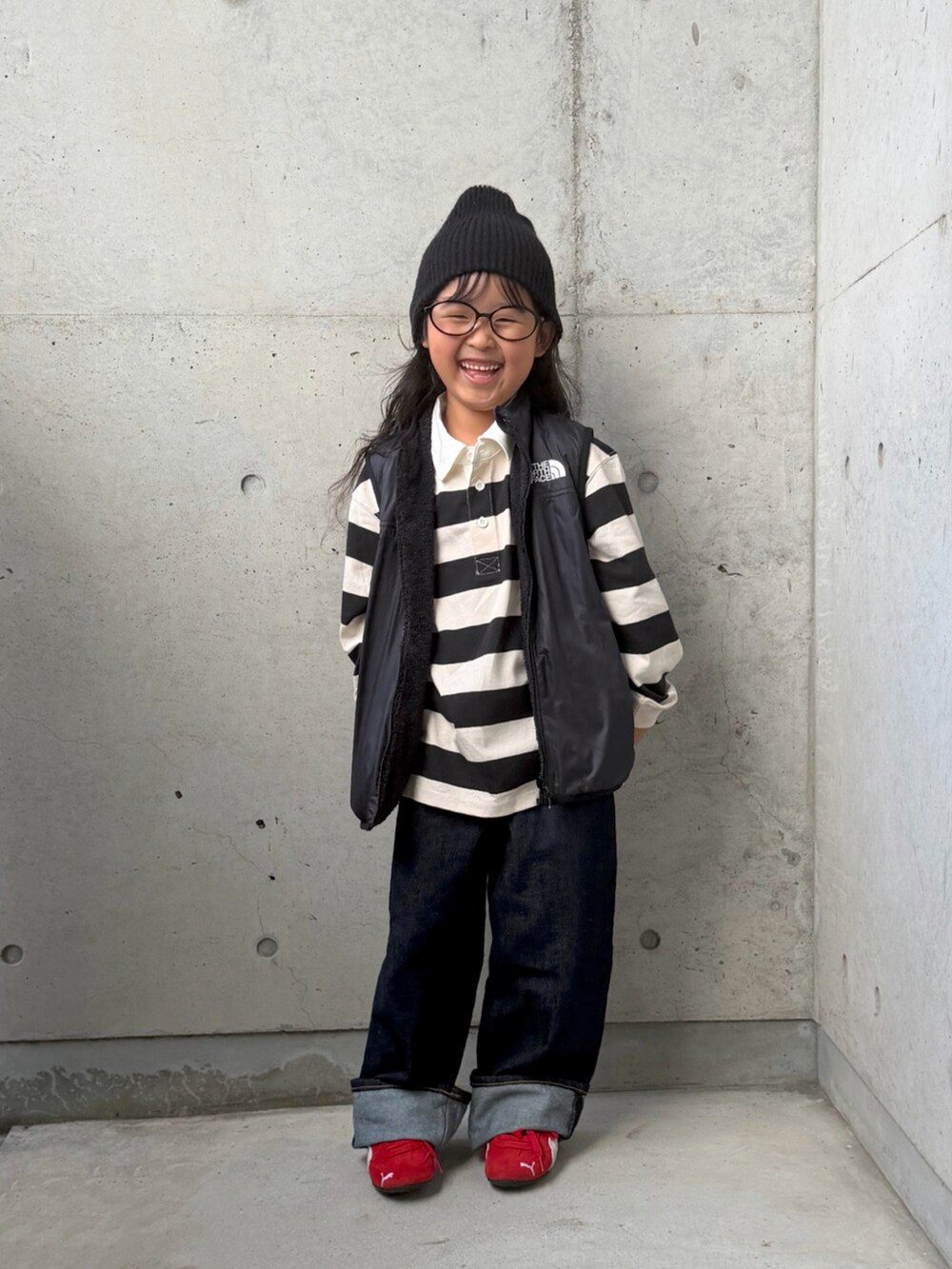 レッド系のスニーカー、ブラック系のベスト、ホワイト系のポロシャツを着用したキッズの秋コーディネートの2枚目の写真