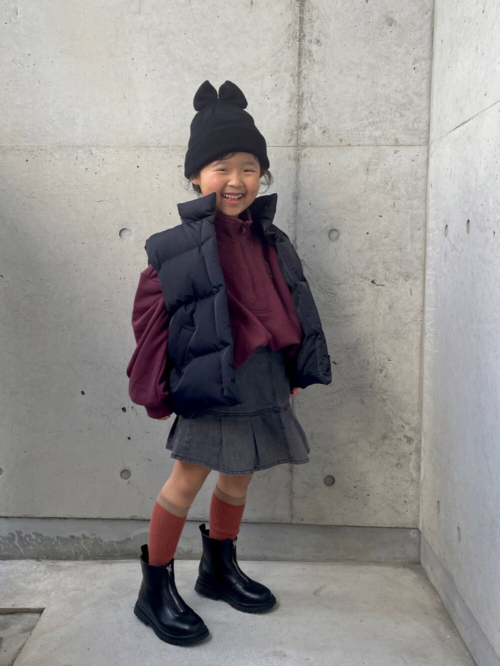 レッド系のスウェット、ブラック系のダウンベスト、ブラック系のブーツを着用したキッズの冬コーディネートの4枚目の写真