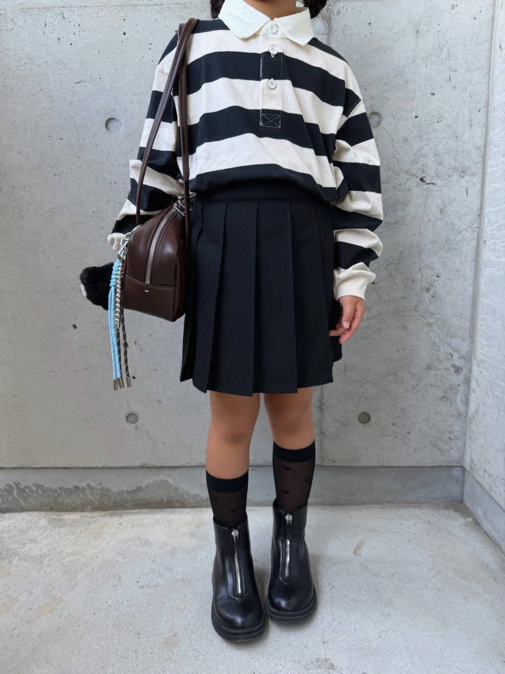 ブラウン系のショルダーバッグ、ブラック系のブーツ、ホワイト系のポロシャツを着用したキッズの秋コーディネートの3枚目の写真