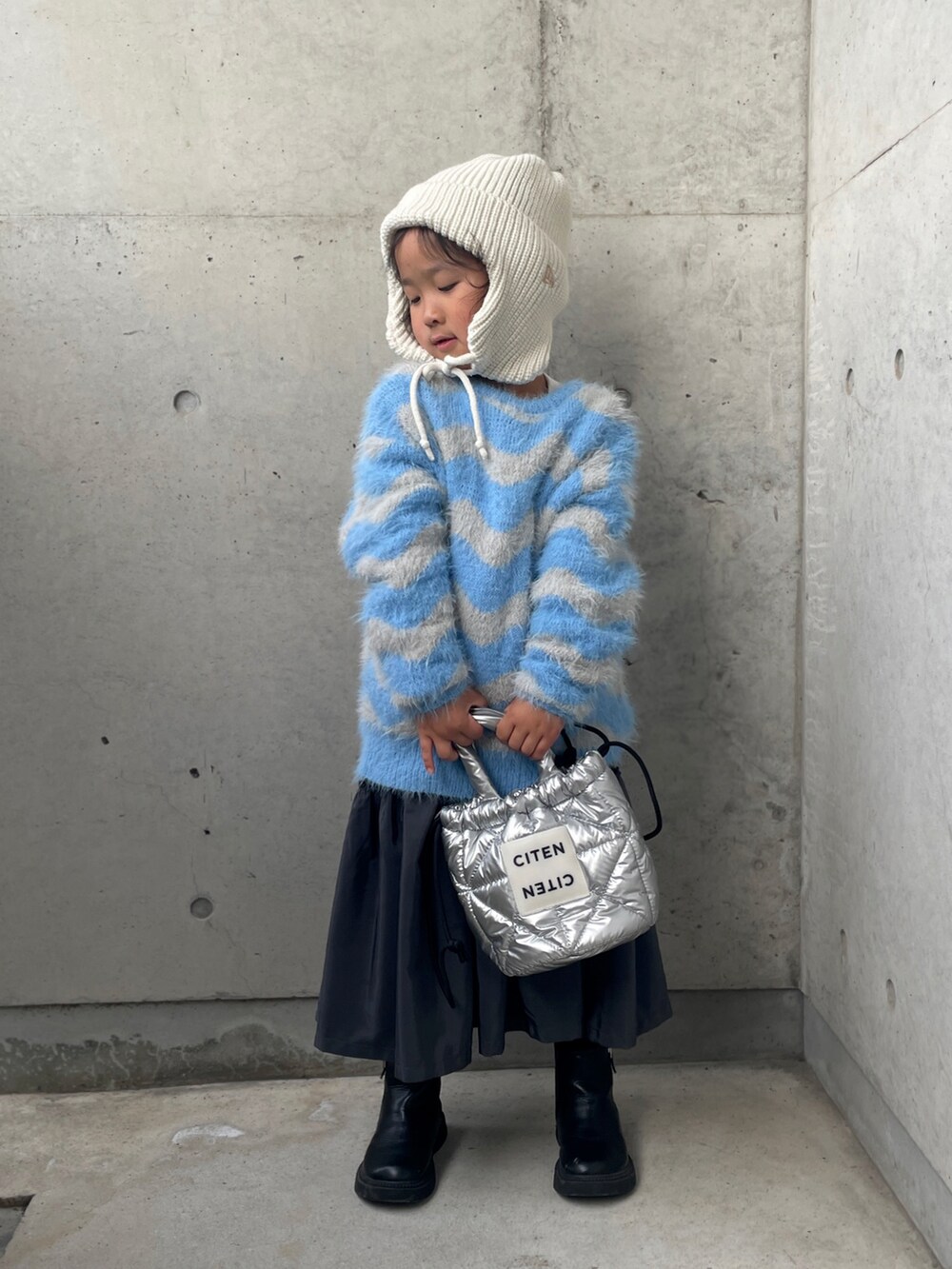 ブルー系のニット/セーター、グレー系のワンピース、シルバー系のトートバッグを着用したキッズの秋コーディネートの2枚目の写真
