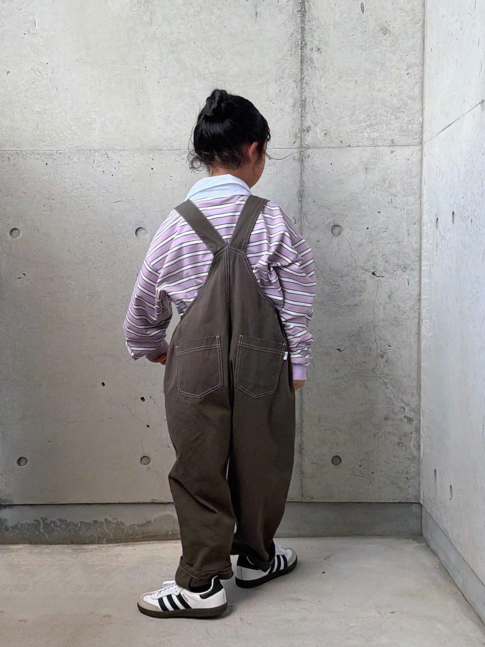 パープル系のポロシャツ、ホワイト系のスニーカー、グレー系のサロペット/オーバーオールを着用したキッズの秋コーディネートの3枚目の写真