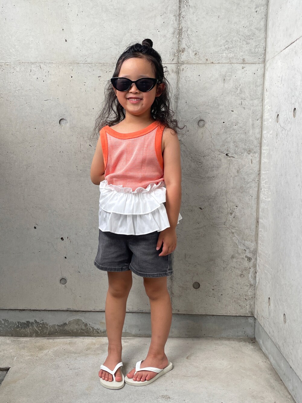 ホワイト系のサンダル、オレンジ系のタンクトップ、グレー系のパンツを着用したキッズの夏コーディネートの5枚目の写真