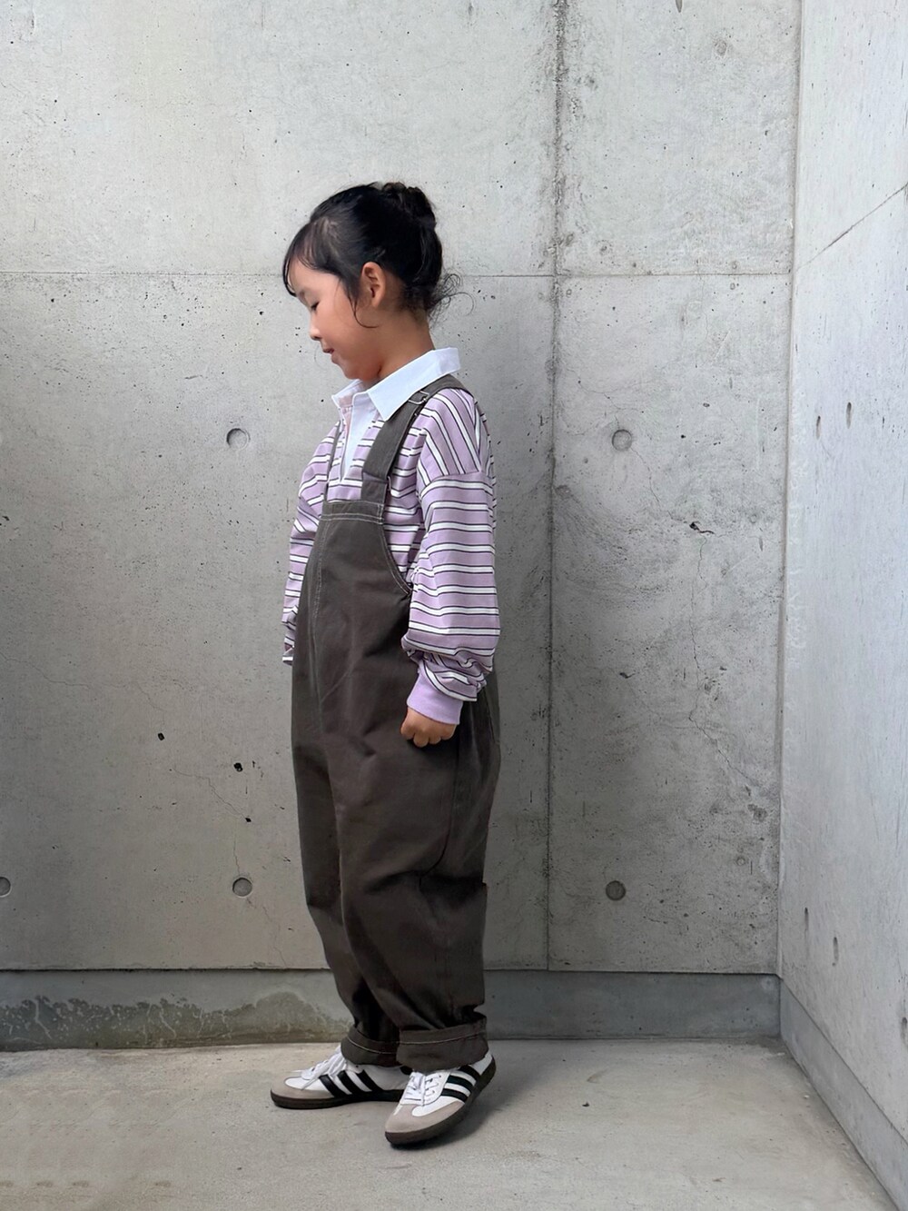 パープル系のポロシャツ、ホワイト系のスニーカー、グレー系のサロペット/オーバーオールを着用したキッズの秋コーディネートの2枚目の写真