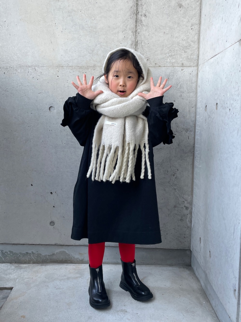 ブラック系のワンピース、ブラック系のブーツ、ホワイト系のマフラーを着用したキッズの冬コーディネートの5枚目の写真