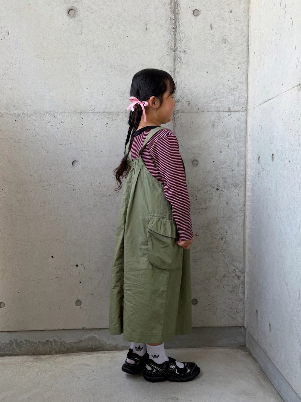 グリーン系のジャンパースカート、ブラック系のサンダル、レッド系のTシャツ/カットソーを着用したキッズの春コーディネートの4枚目の写真
