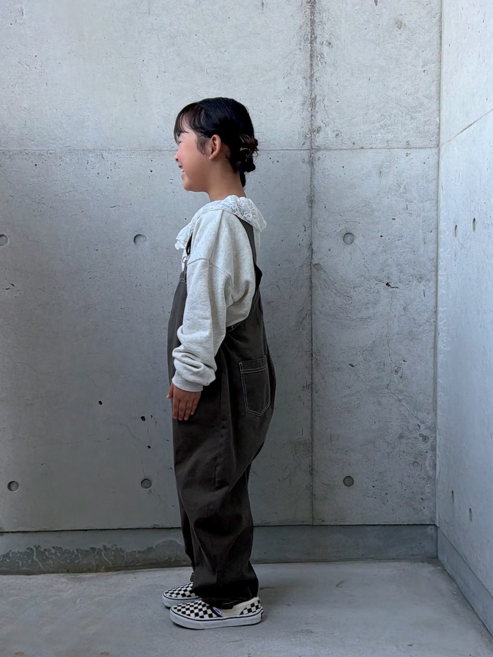 グレー系のサロペット/オーバーオール、ベージュ系のスウェット、ブラック系のスリッポンを着用したキッズの秋コーディネートの2枚目の写真