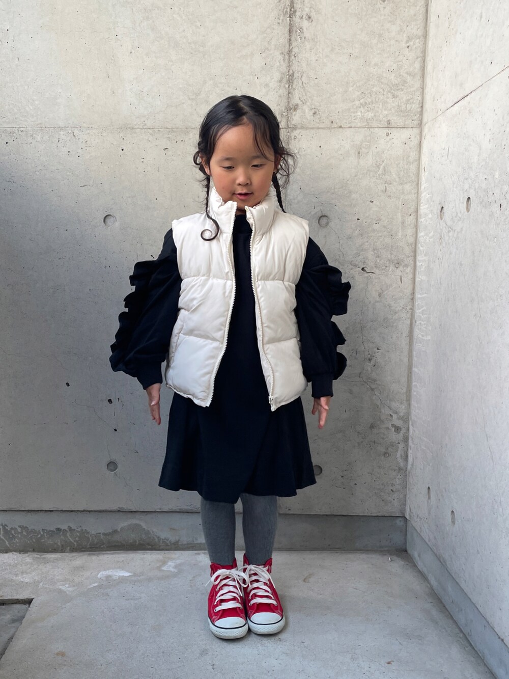 ホワイト系のダウンベスト、ブラック系のワンピース、レッド系のスニーカーを着用したキッズの秋コーディネートの2枚目の写真