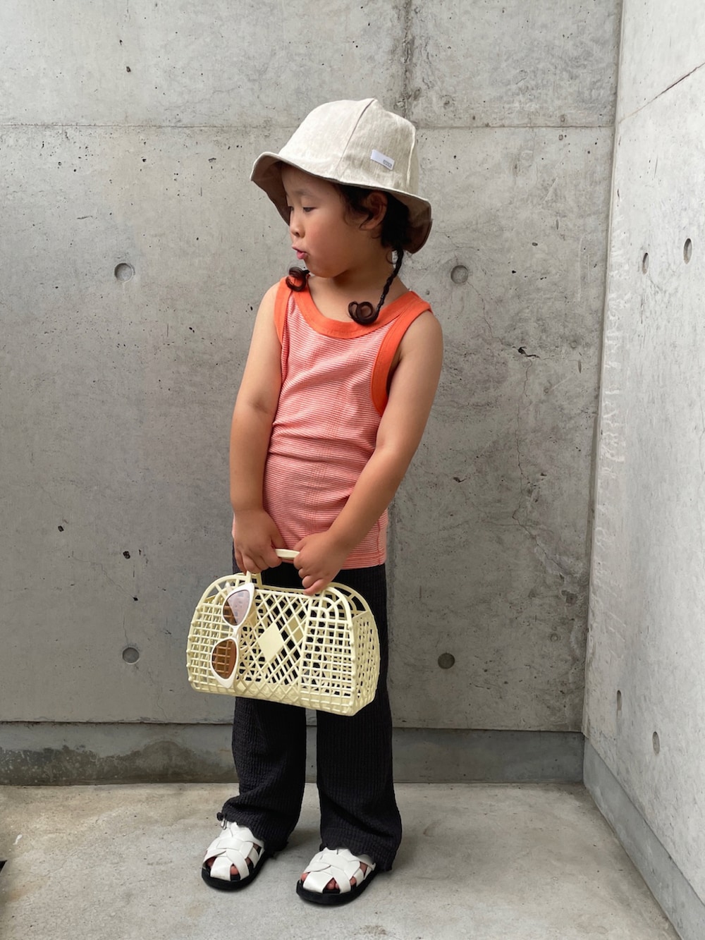 オレンジ系のタンクトップ、グレー系のその他パンツ、ホワイト系のバッグを着用したキッズの夏コーディネートの4枚目の写真