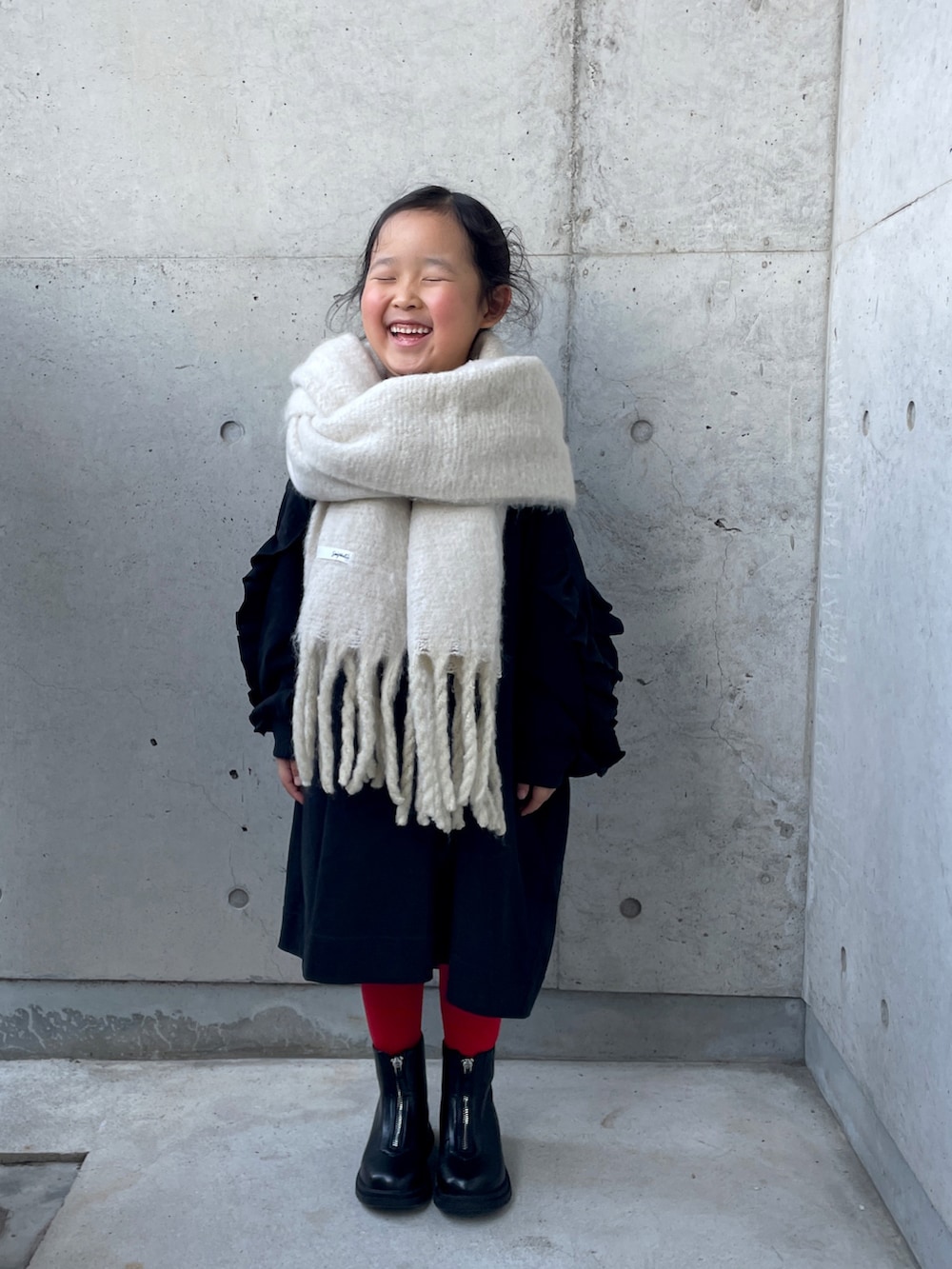 ブラック系のワンピース、ブラック系のブーツ、ホワイト系のマフラーを着用したキッズの冬コーディネートの3枚目の写真