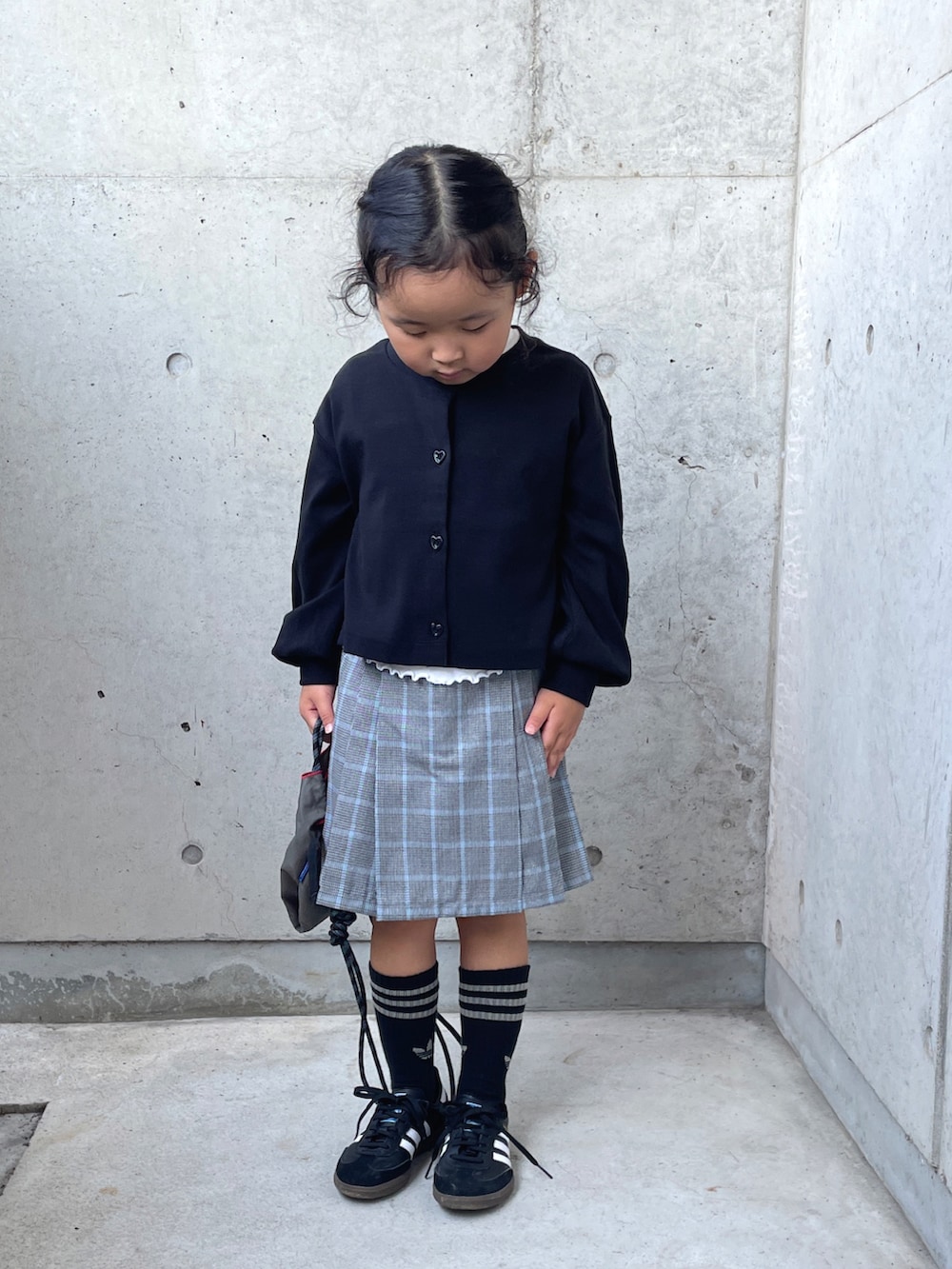 レッド系のパンツ、ブラック系のカーディガン/ボレロ、グレー系のショルダーバッグを着用したキッズの秋コーディネートの2枚目の写真