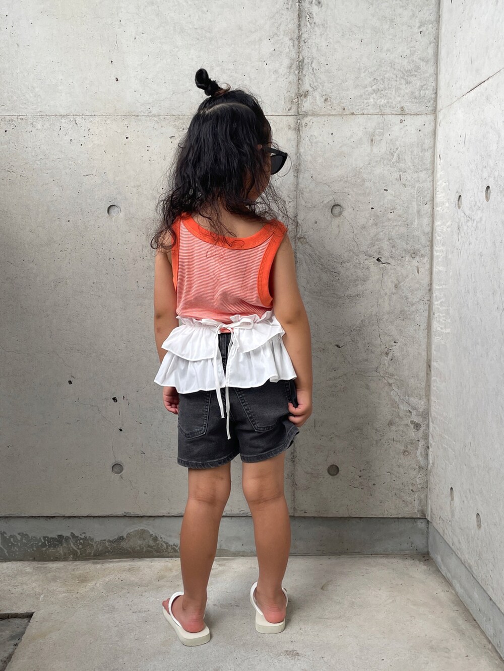 ホワイト系のサンダル、オレンジ系のタンクトップ、グレー系のパンツを着用したキッズの夏コーディネートの4枚目の写真
