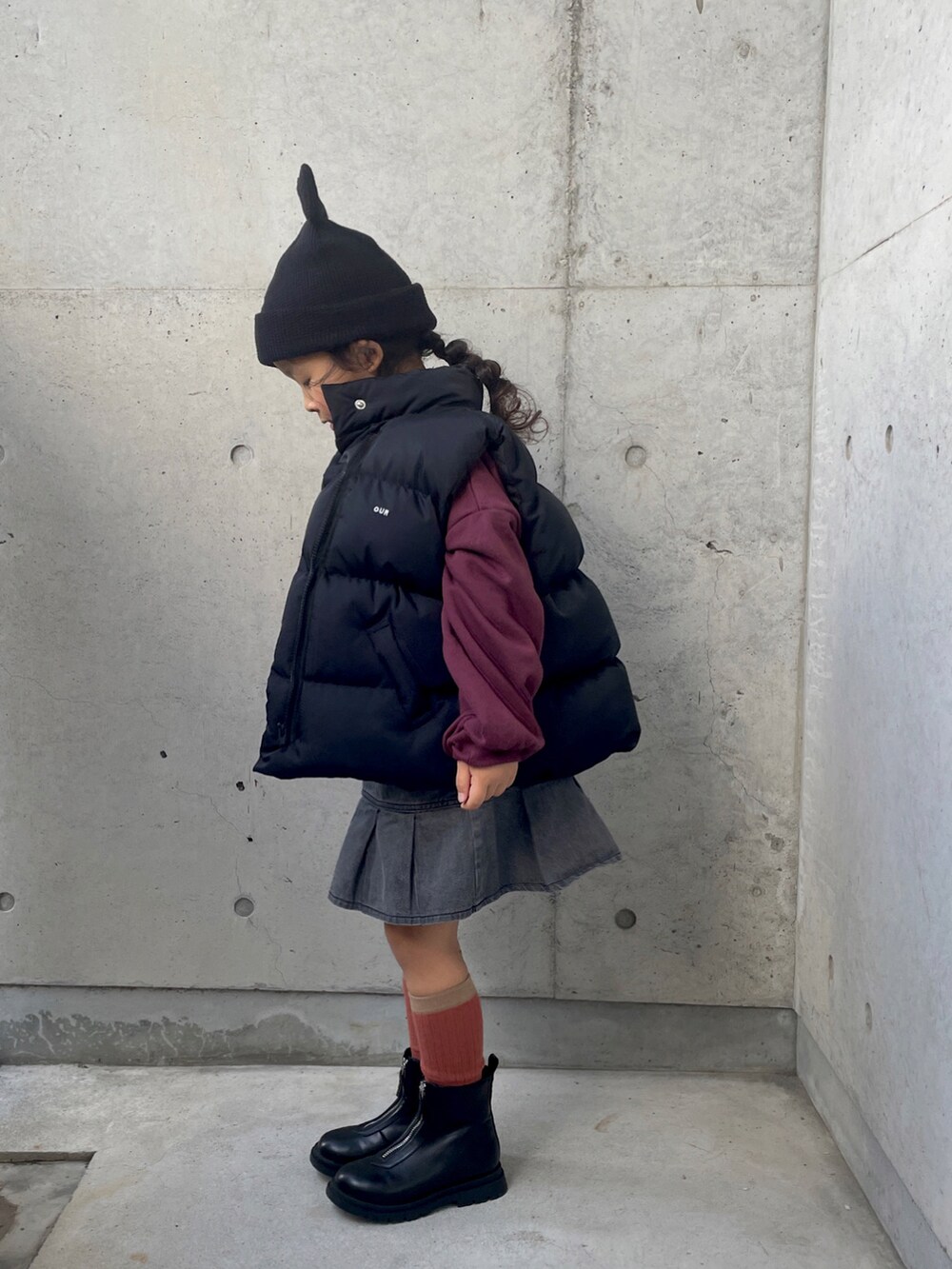 レッド系のスウェット、ブラック系のダウンベスト、ブラック系のブーツを着用したキッズの冬コーディネートの3枚目の写真